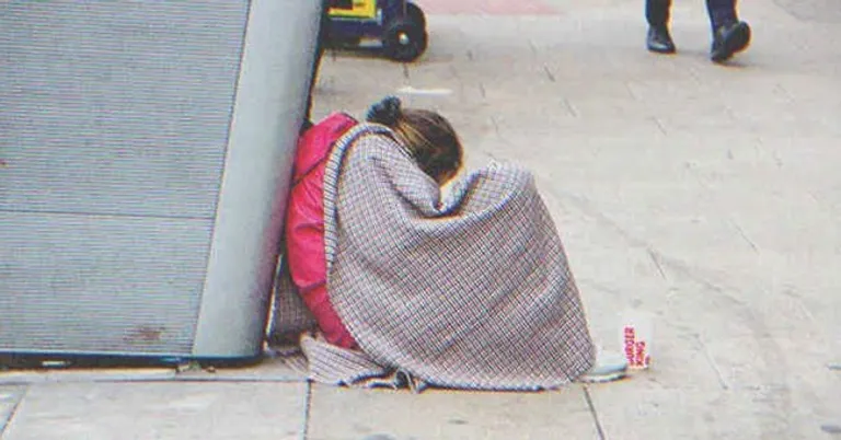 Una joven sin hogar sentada en el suelo cubierta con una manta. | Foto: Shutterstock