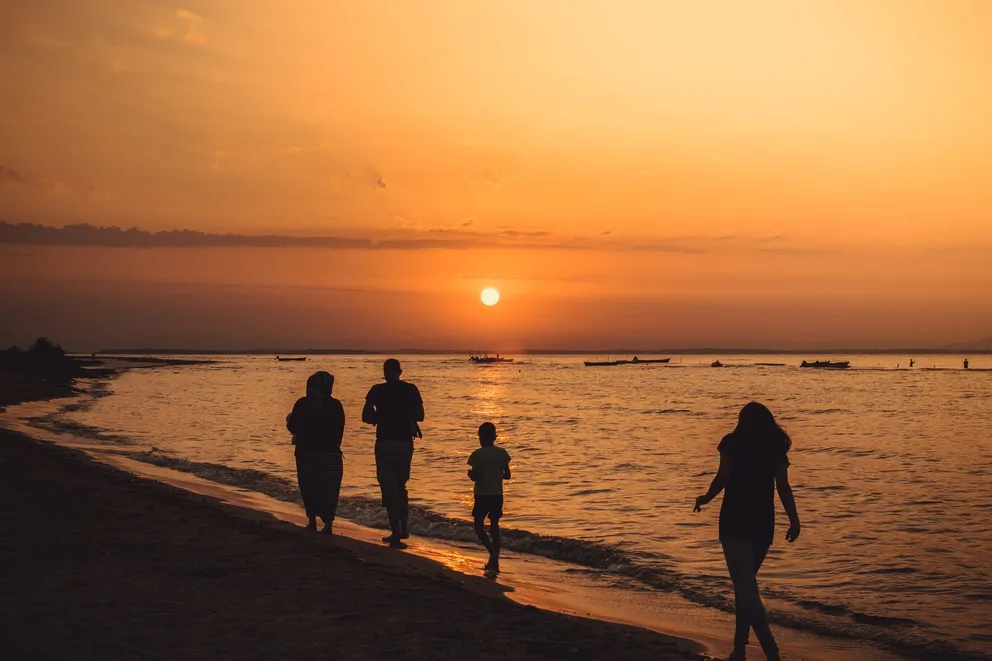 Una familia caminando a orillas de la playa en el atardecer. | Foto: Pexels