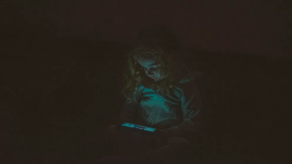 Una niña viendo un teléfono celular en la oscuridad. | Foto: Pexels