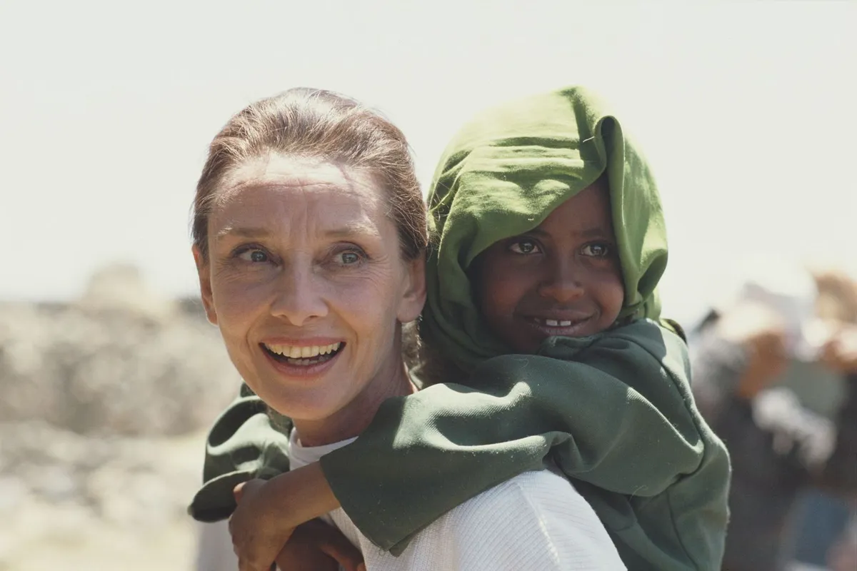 Audrey Hepburn carrying an Ethiopian girl on her back while on her first field mission for UNICEF in Ethiopia, 16th-17th March 1988.| Photo: Getty Images