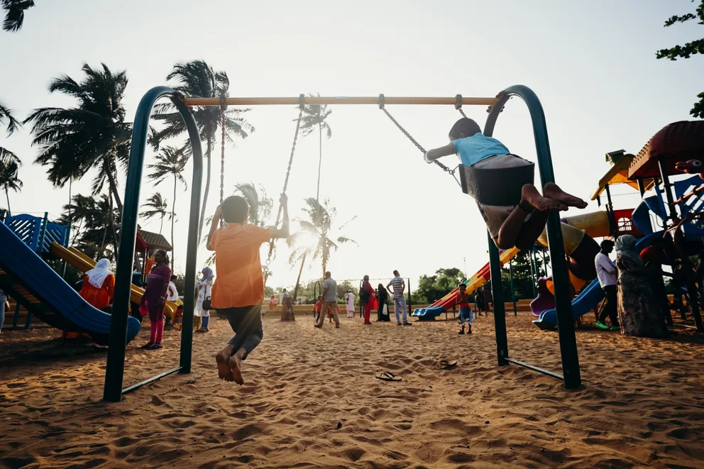Niños jugando en unos columpios sobre la arena. | Foto: Pexels