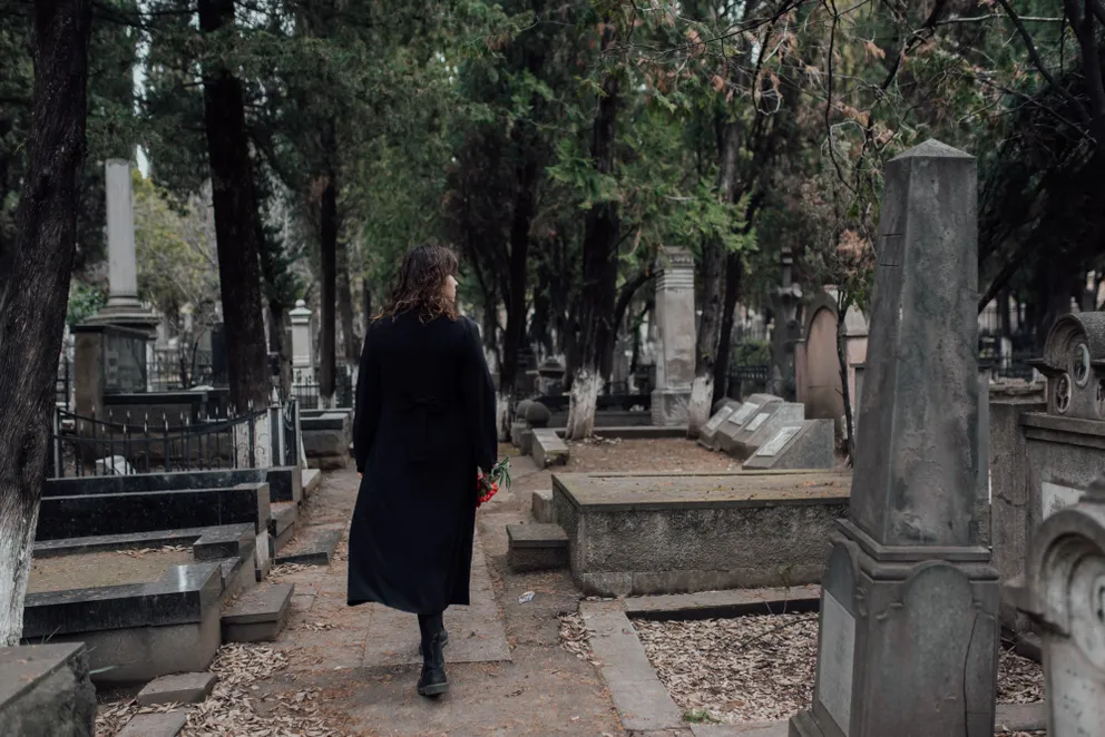 Una mujer vestida de negro caminando entre las tumbas en un cementerio. | Foto: Pexels
