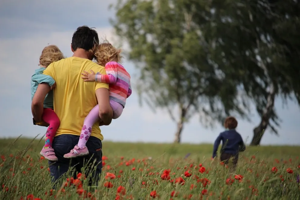 Un hombre jugando con unos niños en un campo con árboles y flores. | Foto: Unsplash