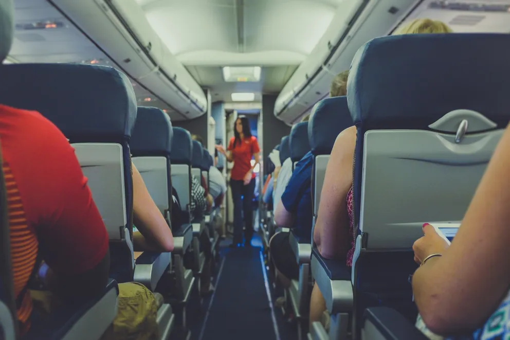 Mujer parada en el pasillo de un avión con pasajeros sentados en los asientos. | Foto: Unsplash