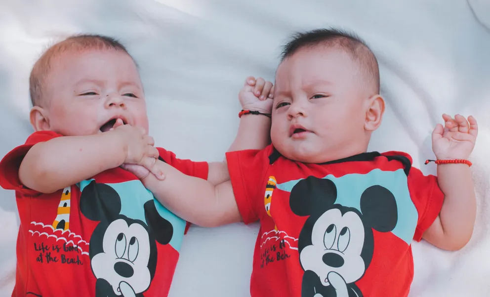 Dos bebés gemelos recostados sobre una cama. | Foto: Pexels