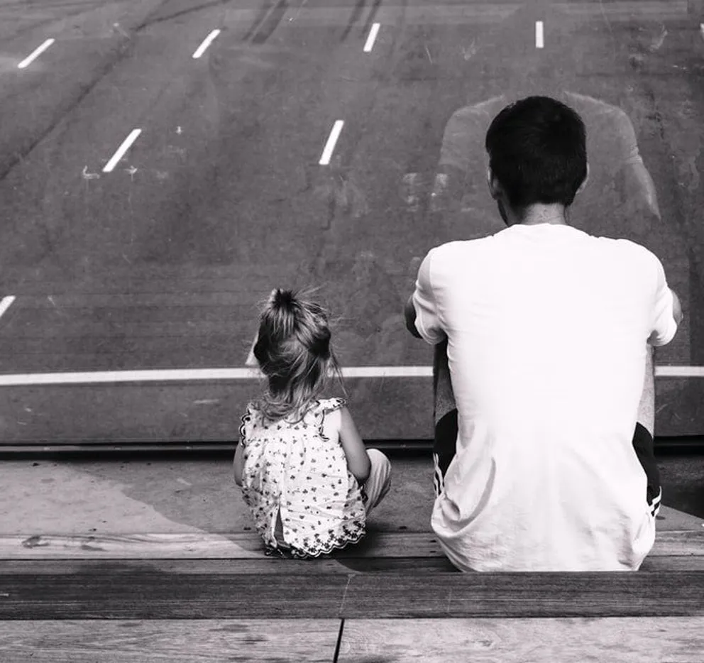Une petite fille assise avec son père | Photo : Pexels