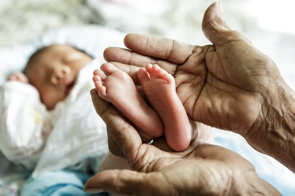 Una mujer mayor sosteniendo los pies de un bebé entre sus manos. | Foto: Shutterstock