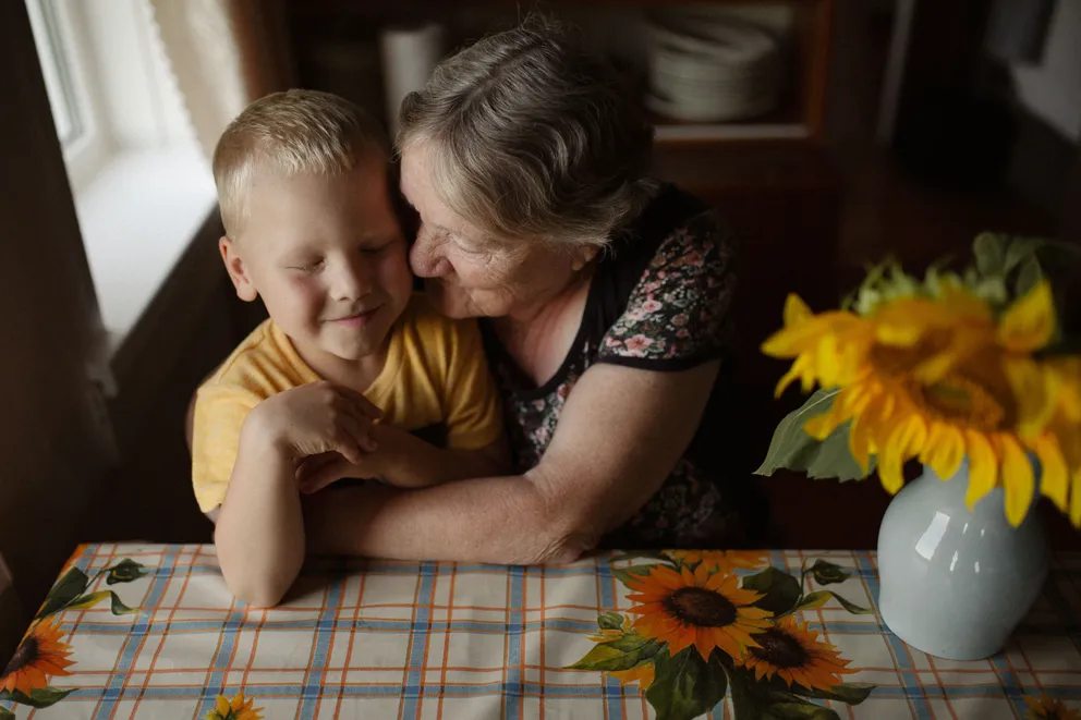 Una mujer mayor abrazando a su nieto sentados frente a una mesa. | Foto: Pexels