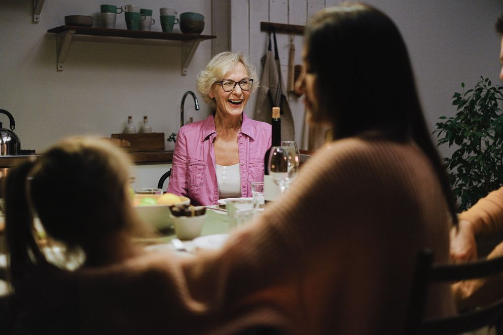 Una mujer mayor sonriente compartiendo con una mujer más joven y una niña alrededor de una mesa. | Foto: Pexels