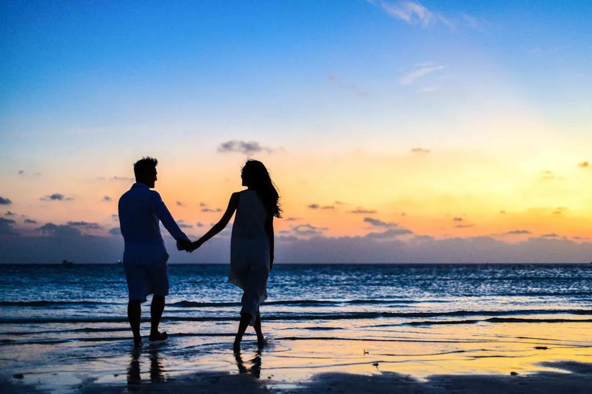 Man and woman holding hands while walking on the seashore. | Photo: Pexels