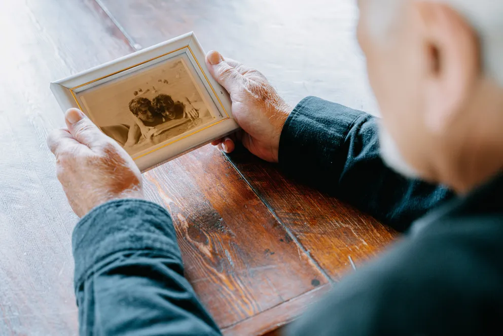 Un anciano observando una fotografía enmarcada. | Foto: Pexels
