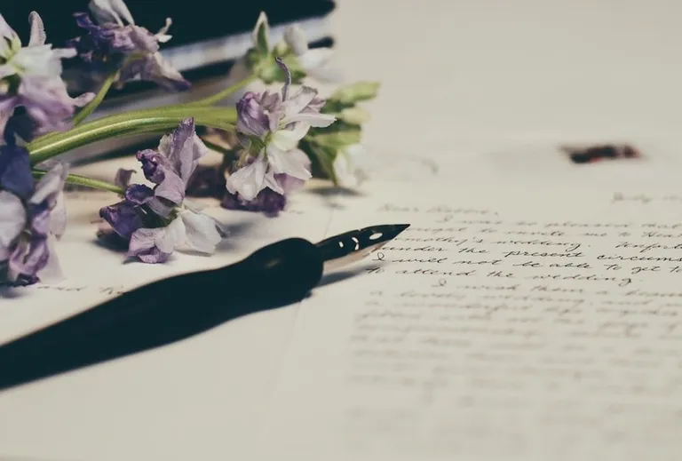 Una pluma fuente junto a unas flores sobre una carta escrita a mano. | Foto: Unsplash