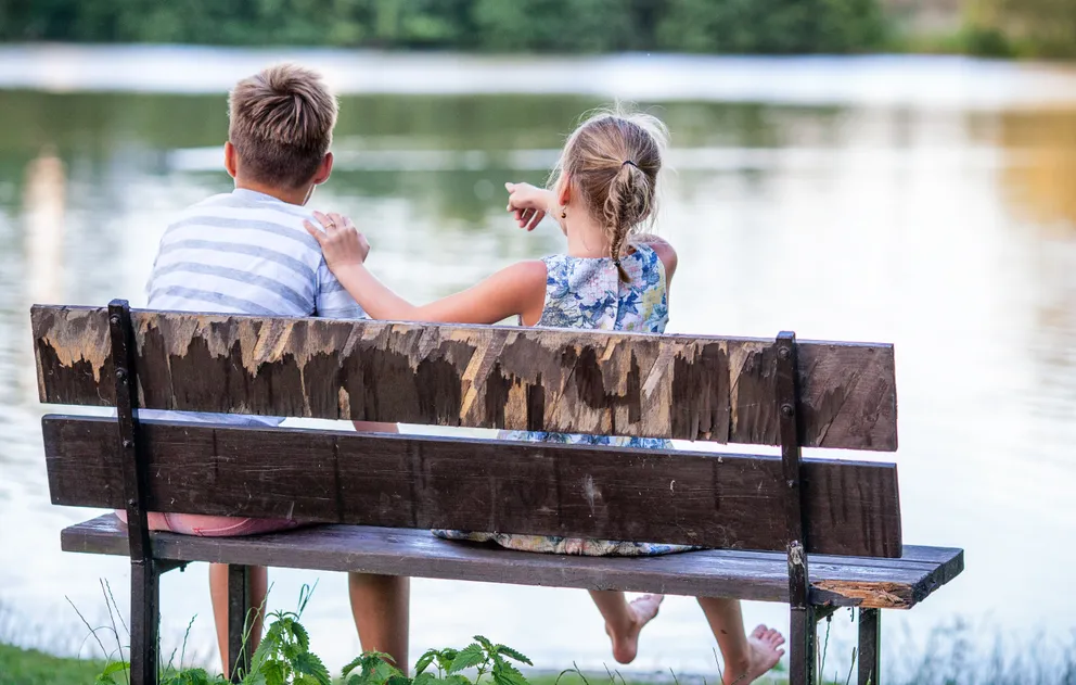 Dos niños sentados sobre un banquillo frente a un lago. | Foto: Pexels