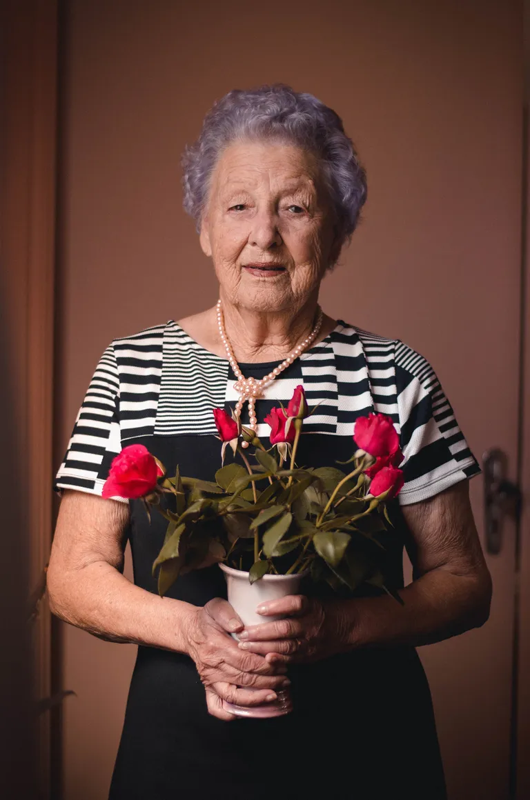 Una anciana sosteniendo un pote con rosas. | Foto: Pexels