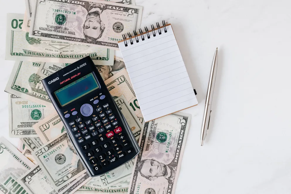 Varios billetes tirados junto a una calculadora, una libreta y un bolígrafo sobre una mesa. | Foto: Pexels