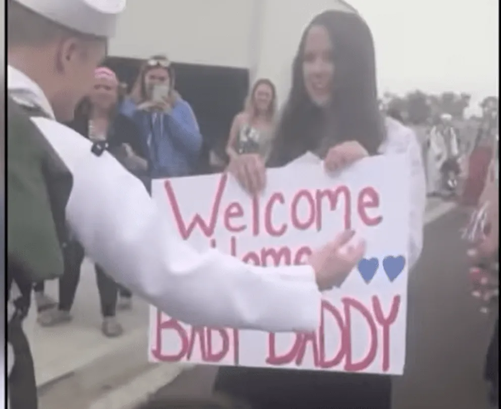 Natasha greets husband Chris with a sign covering her baby bump.  |  Source: youtube.com/CBC Docs