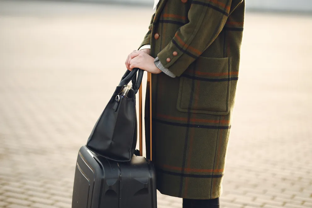 Una mujer sosteniendo una maleta y un bolso. | Foto: Pexels