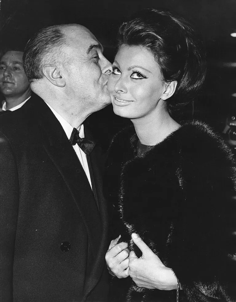 El productor de cine Carlo Ponti besa a su esposa, Sophia Loren, después de que ella recibiera el primer premio Alexander Korda, nombrándola 'Estrella internacional del año', en el estreno mundial de su película 'Lady L' en The Empire, el 26 de noviembre de 1965. | Foto: Getty Images