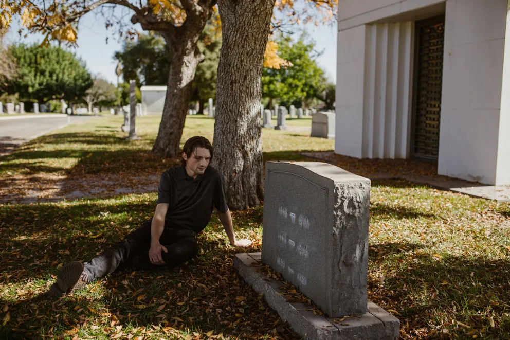 Un joven sentado cerca de una tumba en un cementerio. | Foto: Pexels