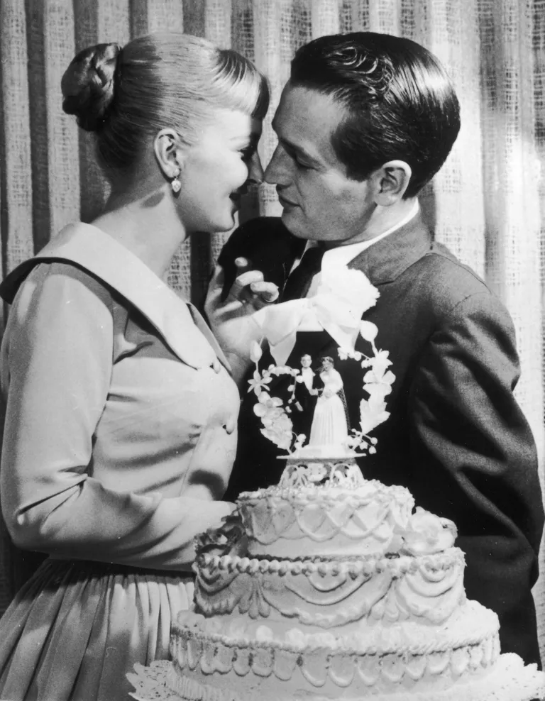 Les jeunes mariés Paul Newman et Joanne Woodward s'embrassent derrière un gâteau de mariage lors de leur réception de mariage à l'hôtel-casino El Rancho, Las Vegas, Nevada, 29 janvier 1958 | Photo : Getty Images