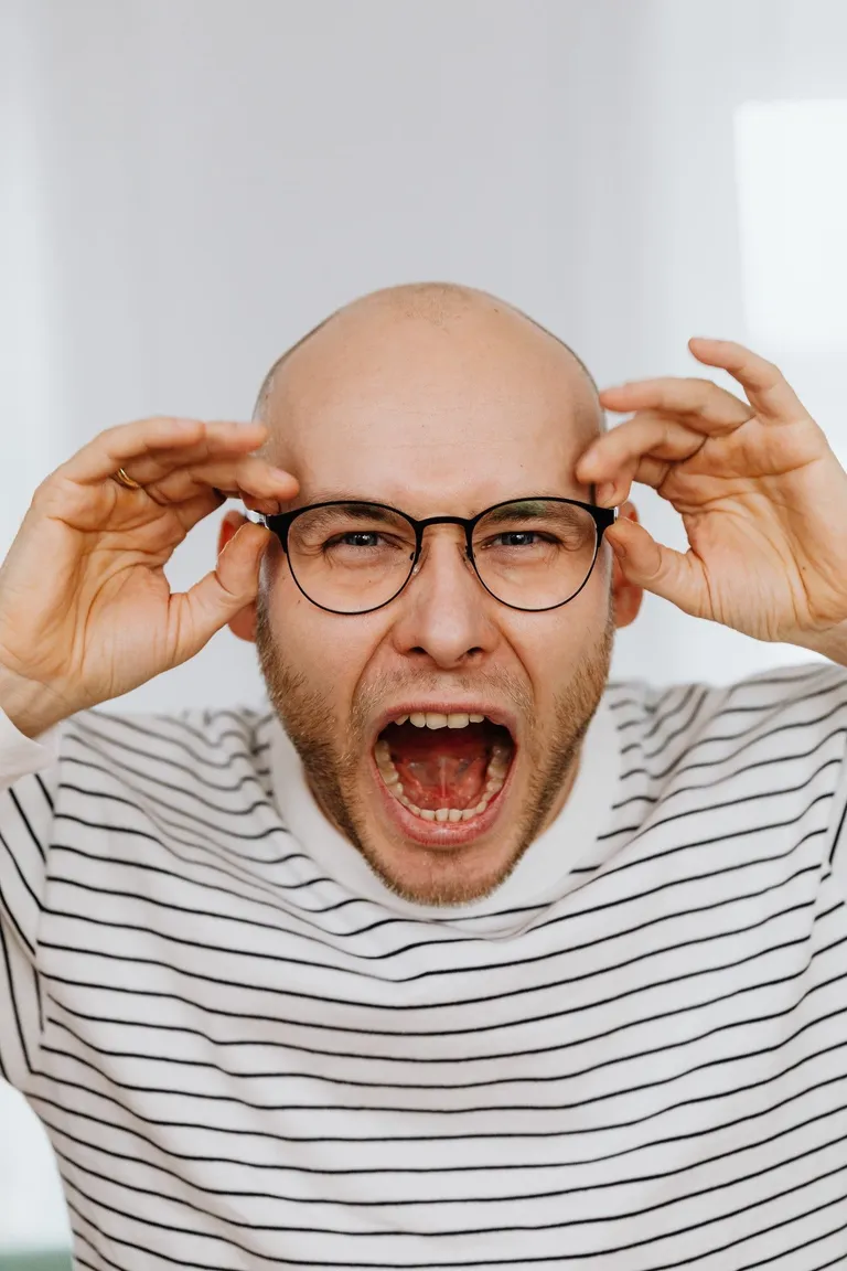 Hombre gritando mientras sostiene sus anteojos. | Foto: Pexels
