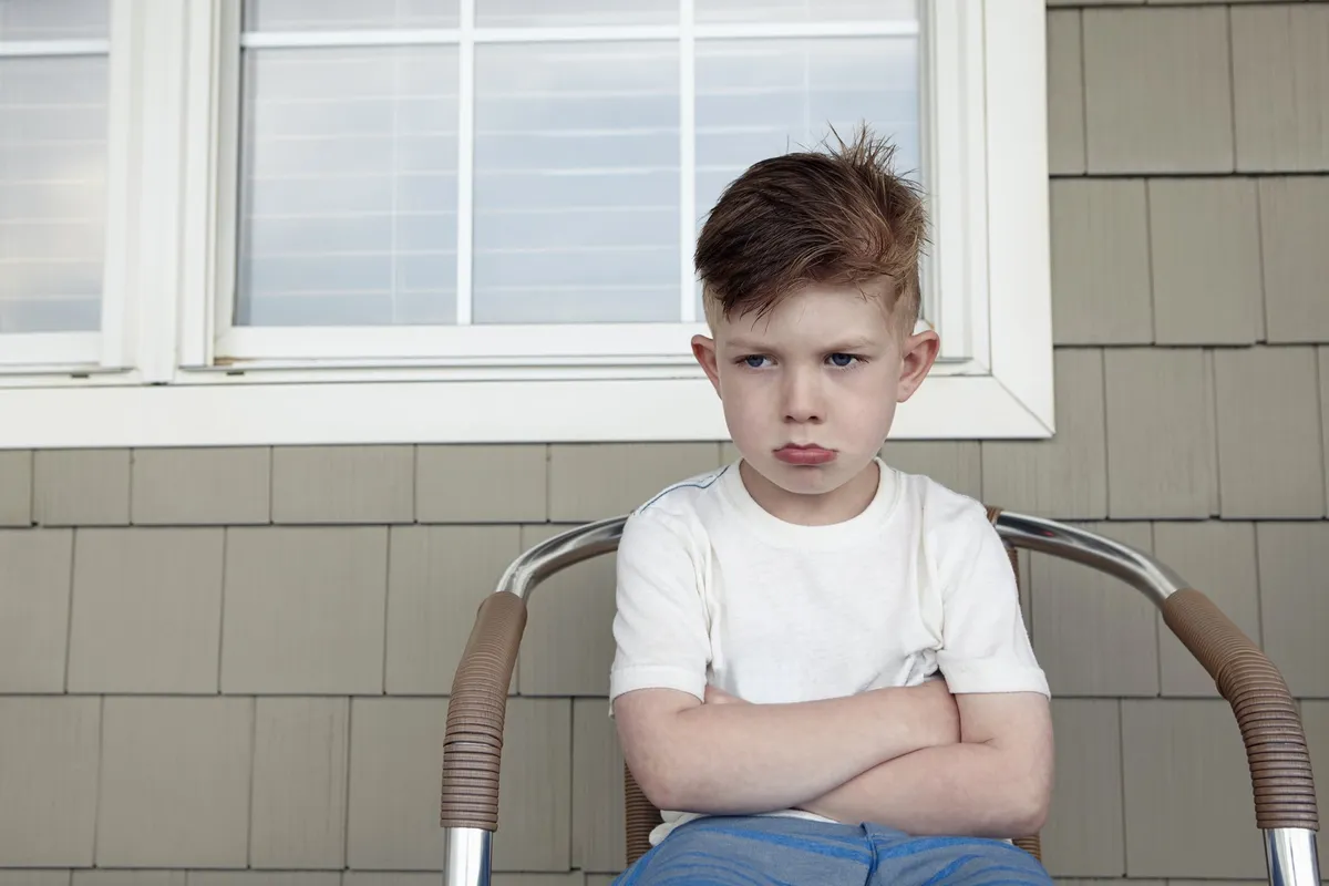 Niño enojado con los brazos cruzados sentado en una silla. | Foto: Getty Images