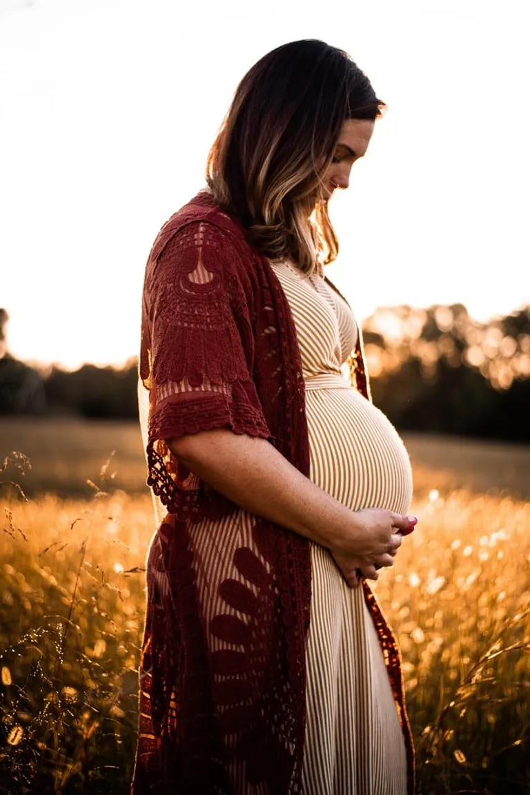 Mujer embarazada sosteniendo su panza en medio de un campo. | Foto: Unsplash