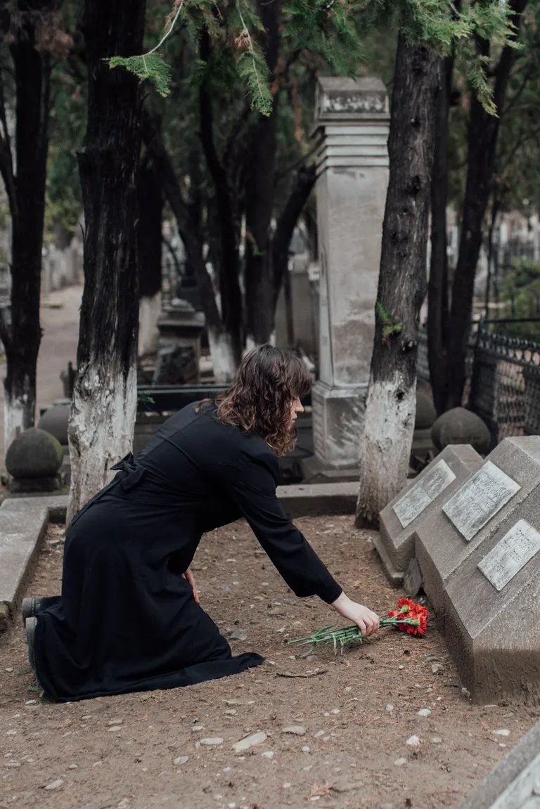 Una mujer de rodillas frente a una tumba. | Foto: Pexels