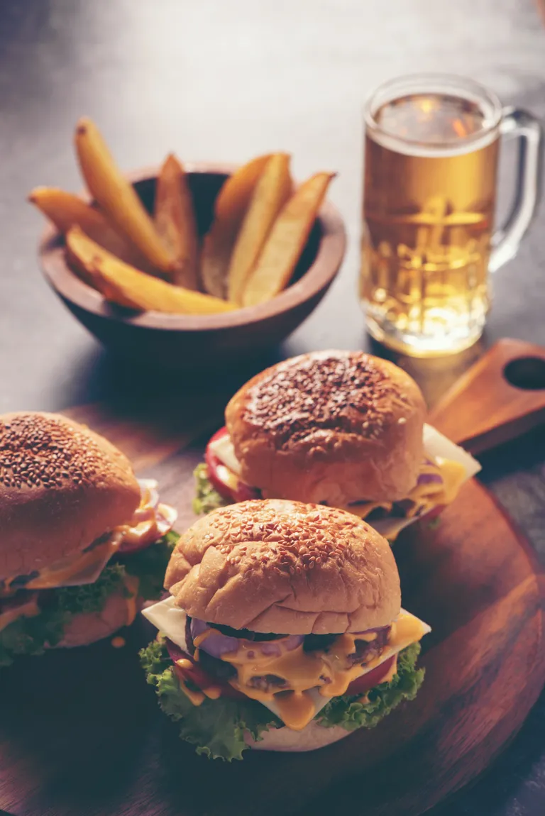 Tres hamburguesas, papas fritas y cerveza sobre una mesa. | Foto: Pexels