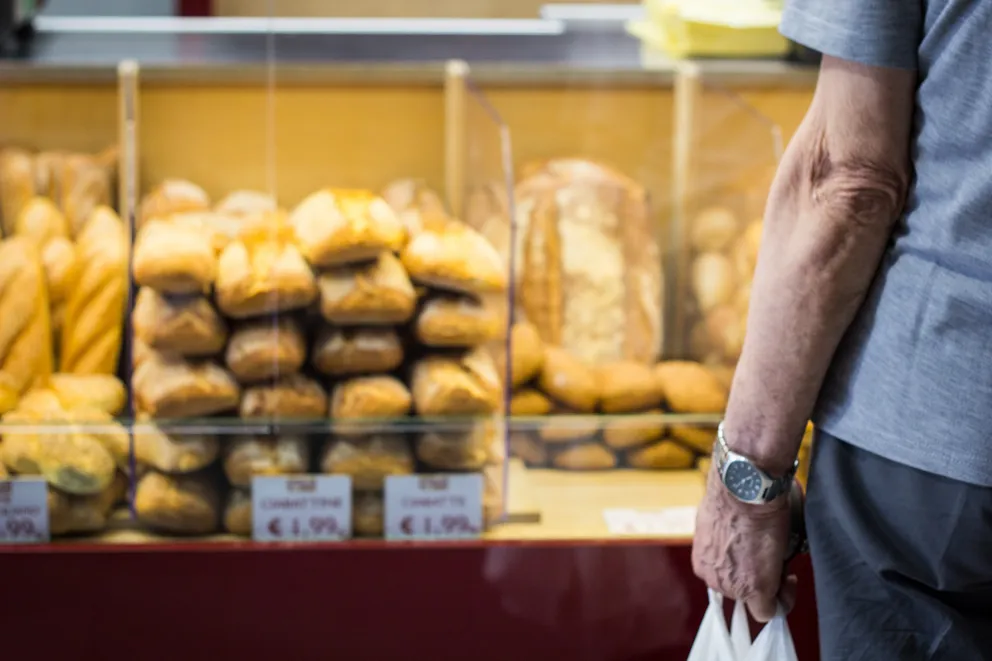 Hombre parado frente a unos mostradores con diferentes tipos de pan. | Foto: Unsplash