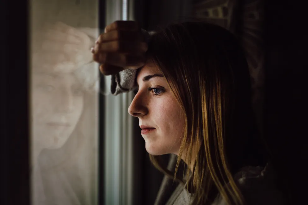 Una mujer con rostro angustiado mirando a través de una ventana. | Foto: Pexels