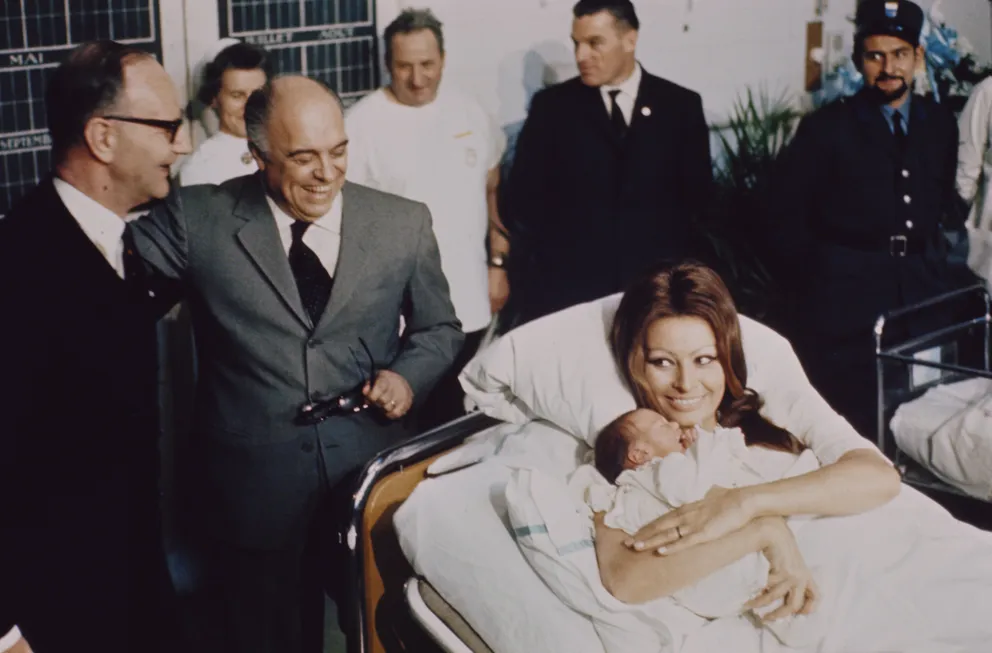 Sophia Loren est allongée sur un lit d'hôpital dans une maternité, tenant dans ses bras son nouveau-né Carlo junior, avec son mari Carlo Ponti à côté du lit, le 4 janvier 1969 à Genève, en Suisse. | Photo : Getty Images