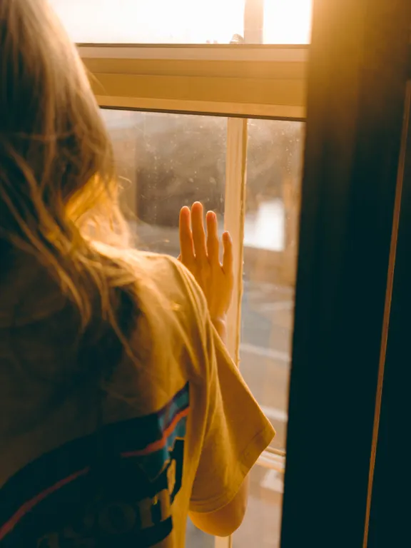 Una joven mirando a través de una ventana con su mano sobre el vidrio. | Foto: Pexels