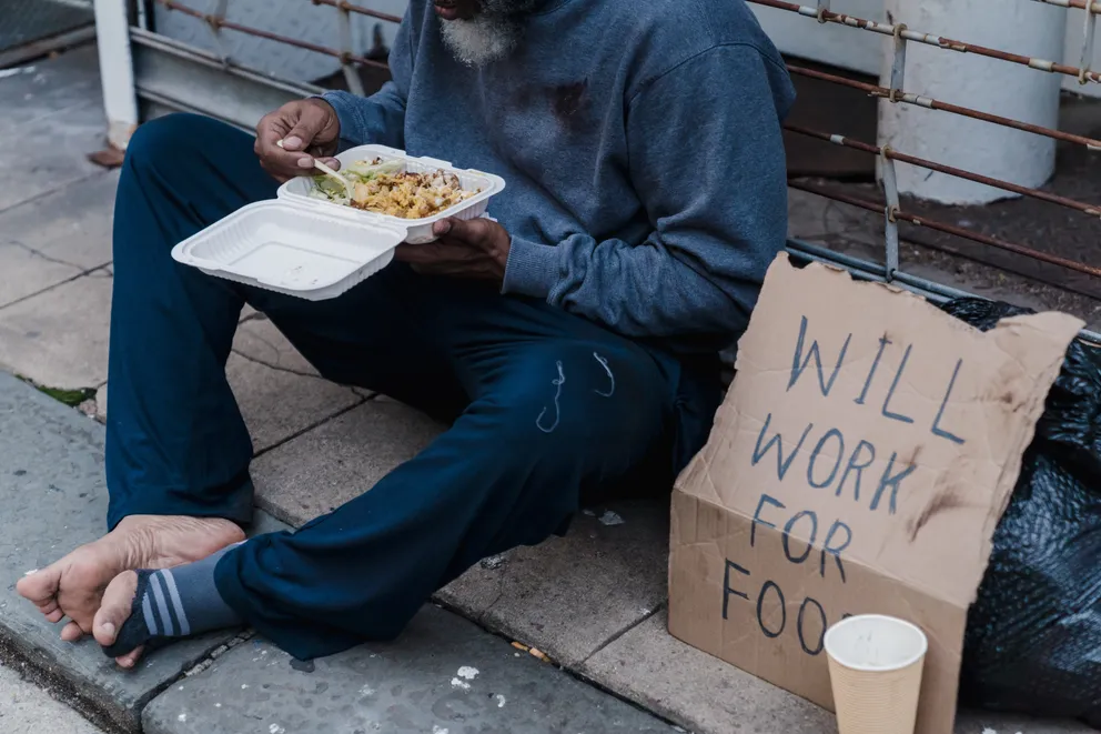 Hombre sin hogar sentado en el suelo comiendo. | Foto: Pexels