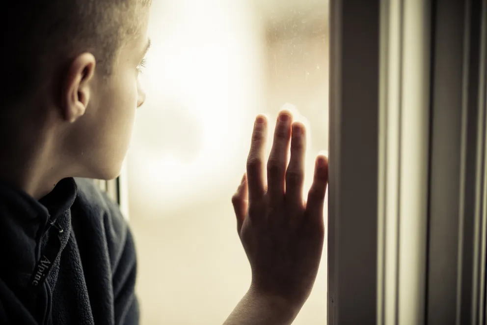 Garçon solitaire regardant par la fenêtre. │Source : Shutterstock