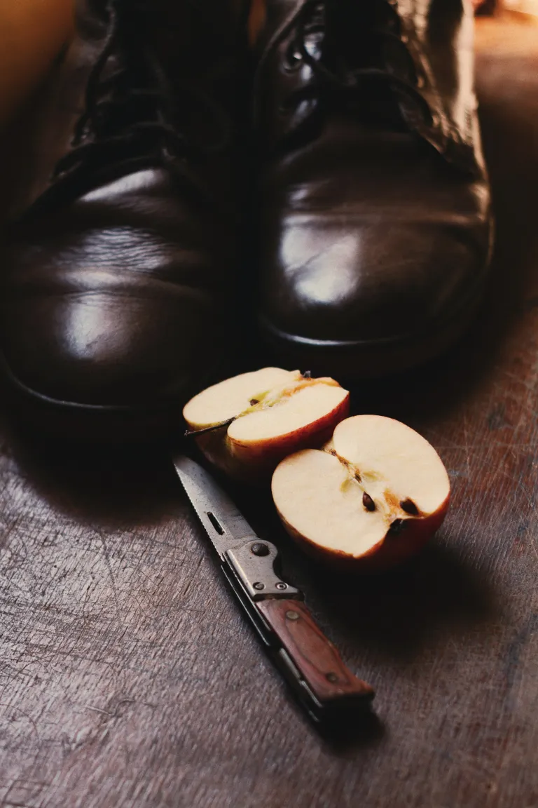 Una navaja junto a una manzana cortada por la mitad y unos zapatos. | Foto: Pexels