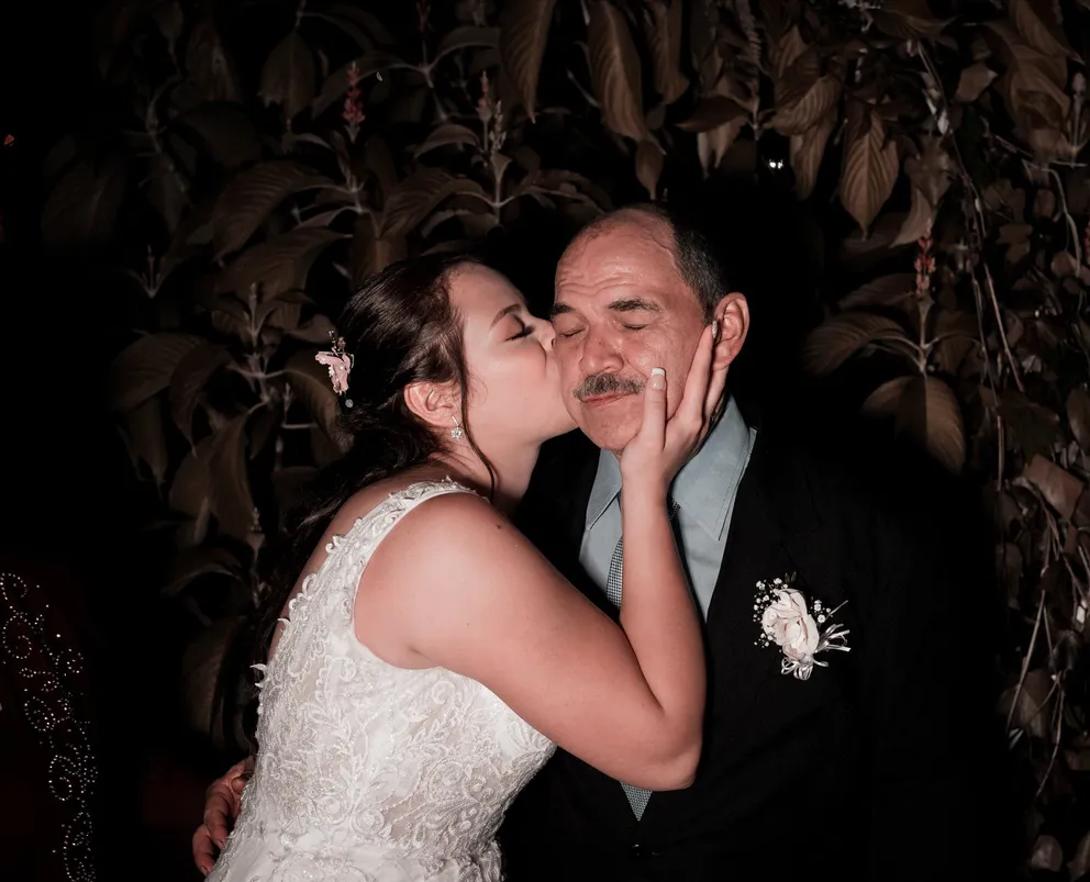Una joven vestida de novia dándole un afectuoso beso en la mejilla a un hombre mayor. | Foto: Pexels