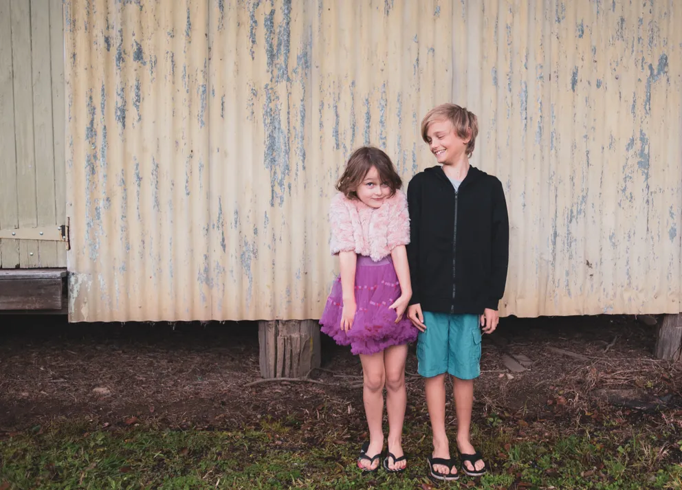 Dos niños sonrientes parados frente a una casa. | Foto: Pexels