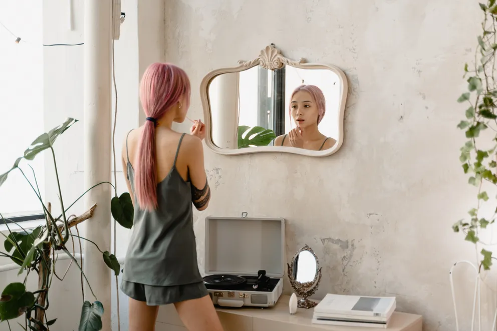 Joven maquillándose frente a un espejo. | Foto: Pexels