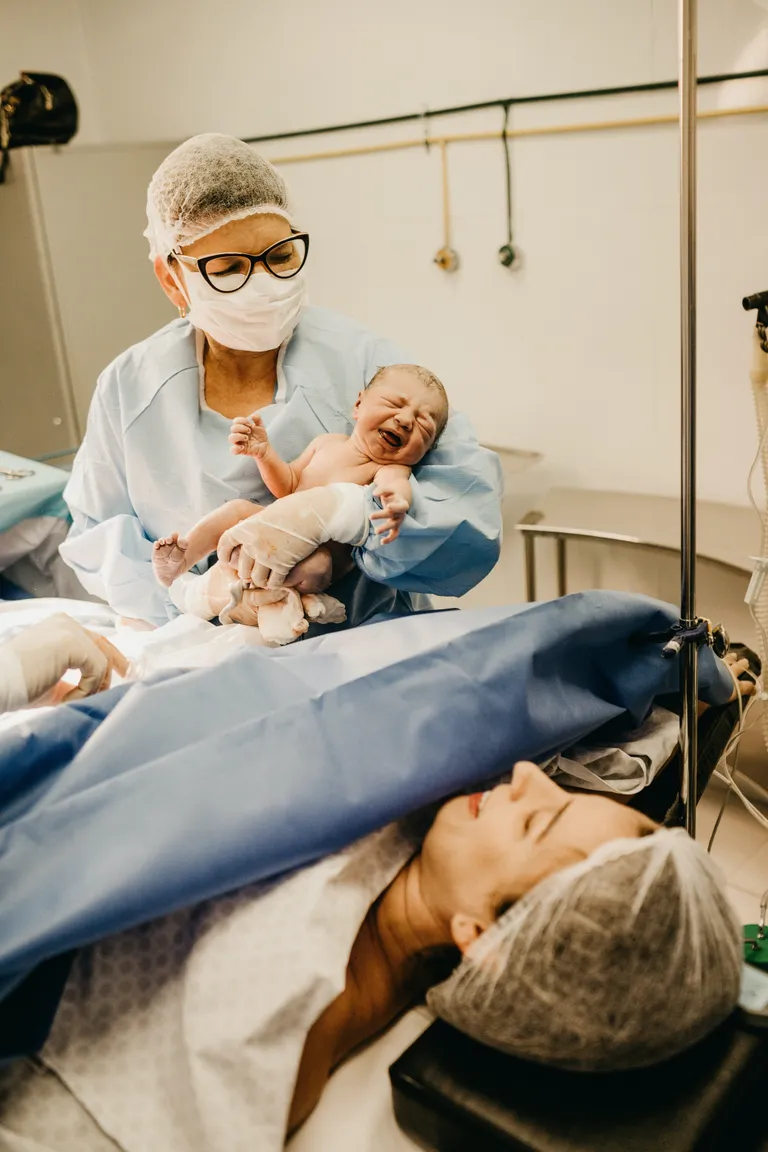Una mujer que acaba de dar a luz y una doctora cargando al bebé recién nacido. | Foto: Pexels