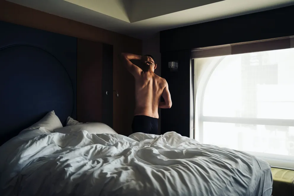 Hombre junto a una cama con la parte superior de su cuerpo descubierta. | Foto: Unsplash