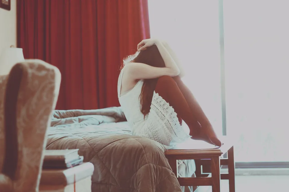 Una joven sentada en una cama con su rostro sobre sus rodillas. | Foto: Unsplash