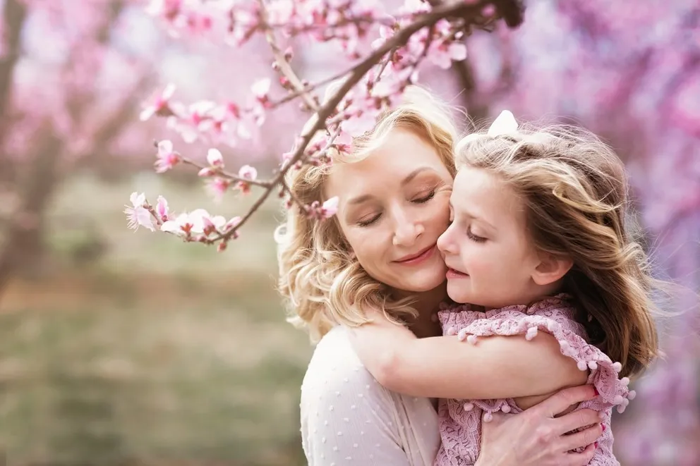 Mujer abrazando a su hija bajo árboles de cerezo. | Foto: Unsplash
