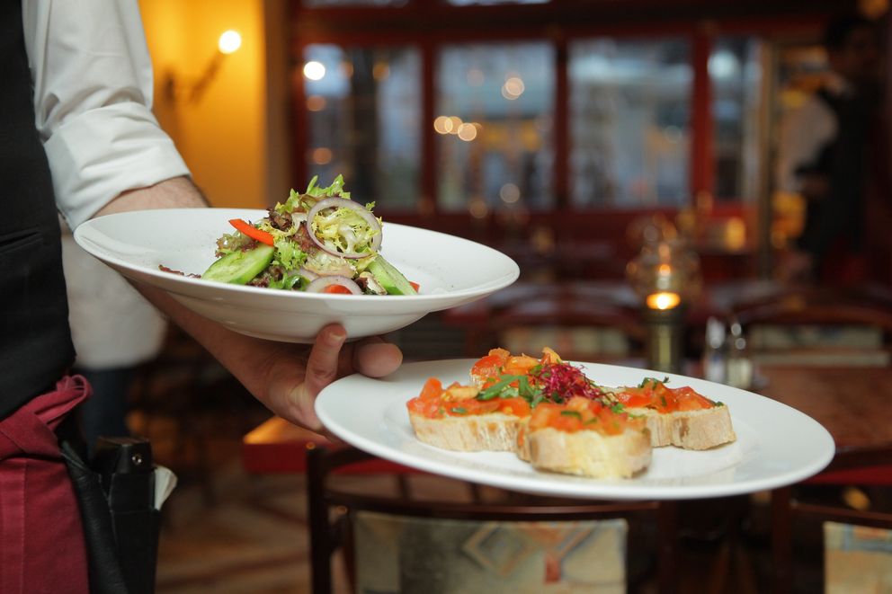 Un camarero llevando dos platos con comida. | Foto: Pexels 