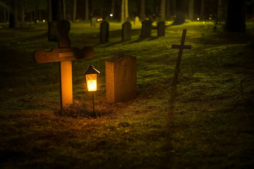 Lápidas junto a un farol en un cementerio durante la noche. | Foto: Pexels 