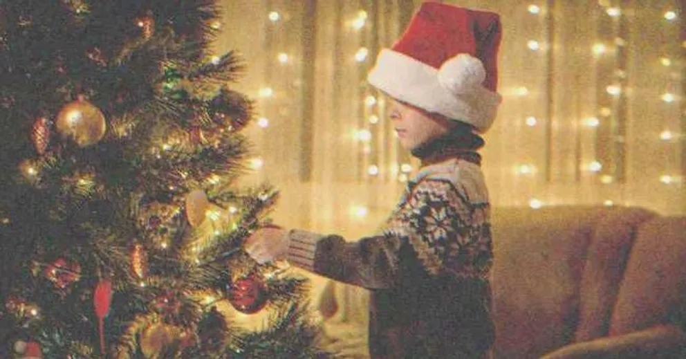 Niño colocando un adorno en un árbol de Navidad. | Foto: Shutterstock