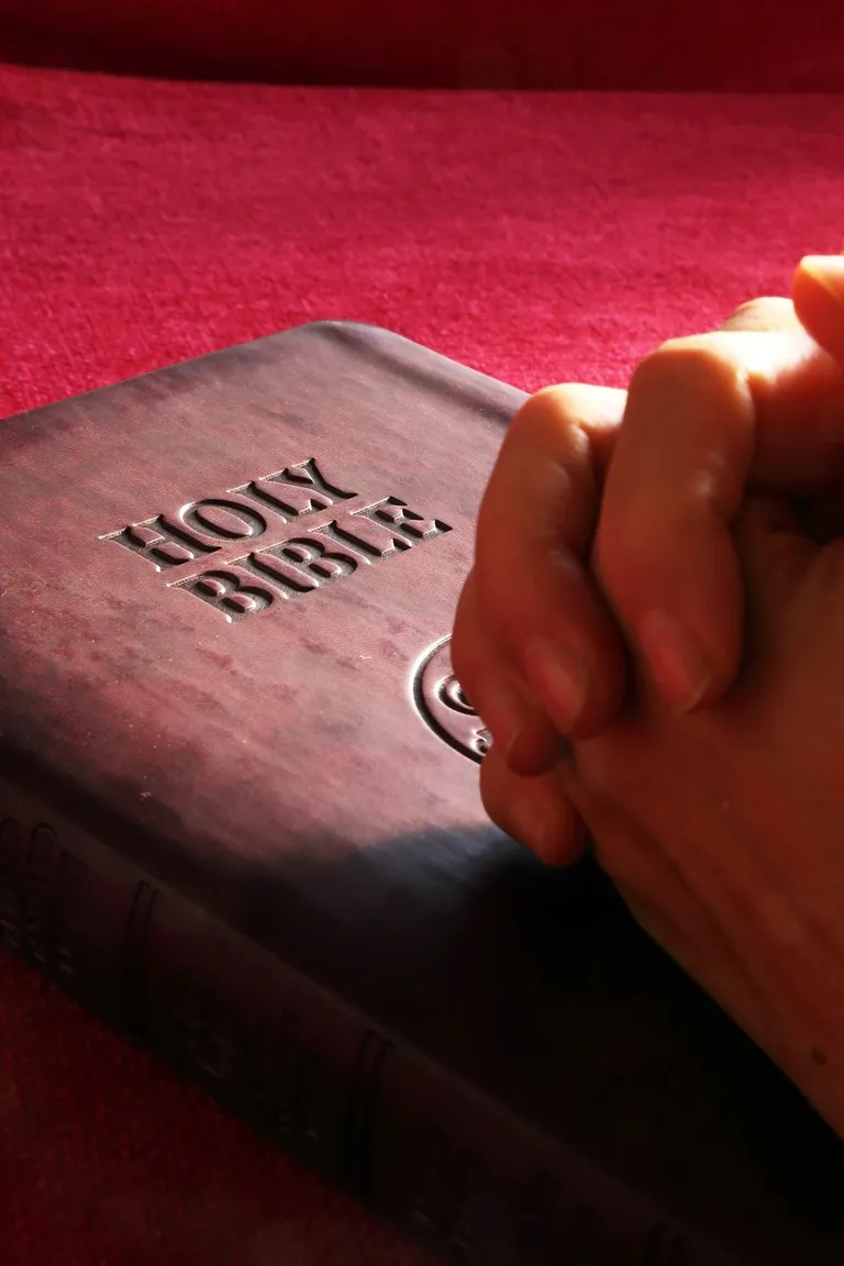 Una persona orando con sus manos sobre una Biblia. | Foto: Pexels
