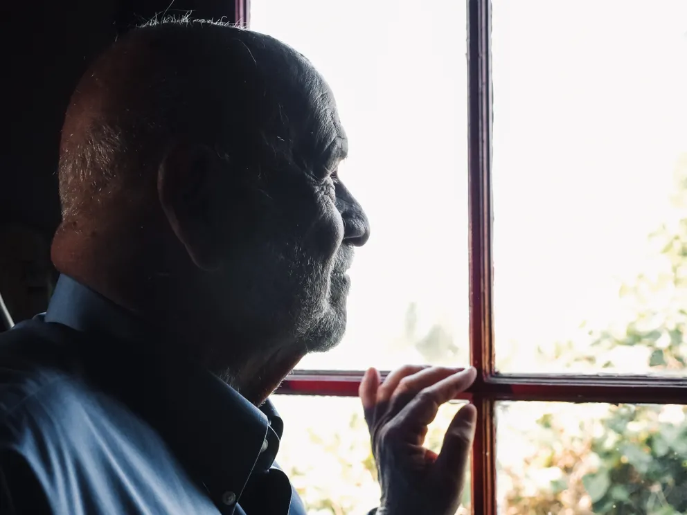 Un hombre mayor mirando a través de una ventana. | Foto: Pexels