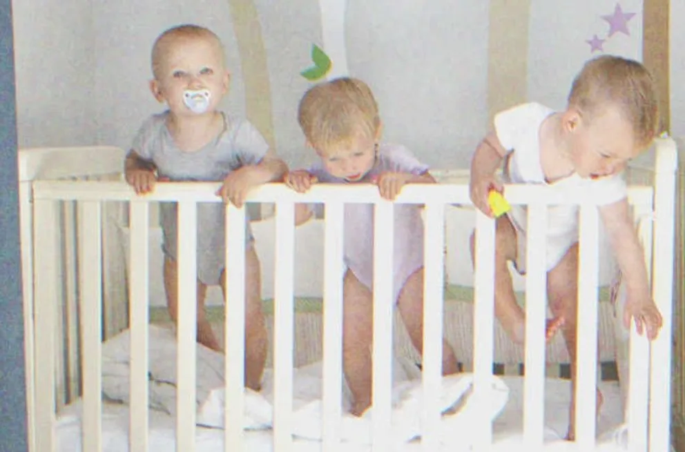 Bebés trillizos parados dentro de una cuna. | Foto: Shutterstock