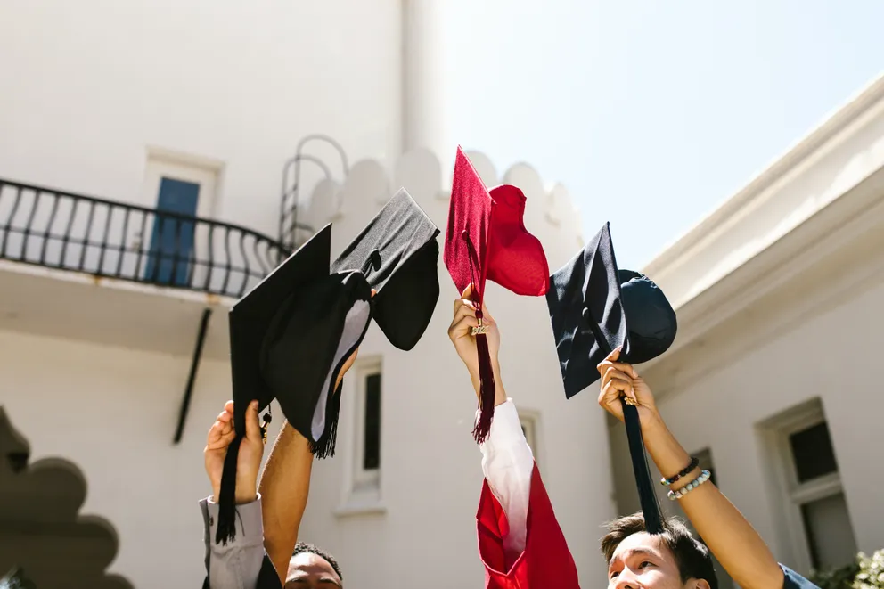 Jóvenes levantando los birretes en sus manos el día de su graduación. | Foto: Pexels